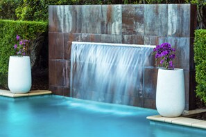Una piscina con una cascata e due grandi fioriere con fiori viola.