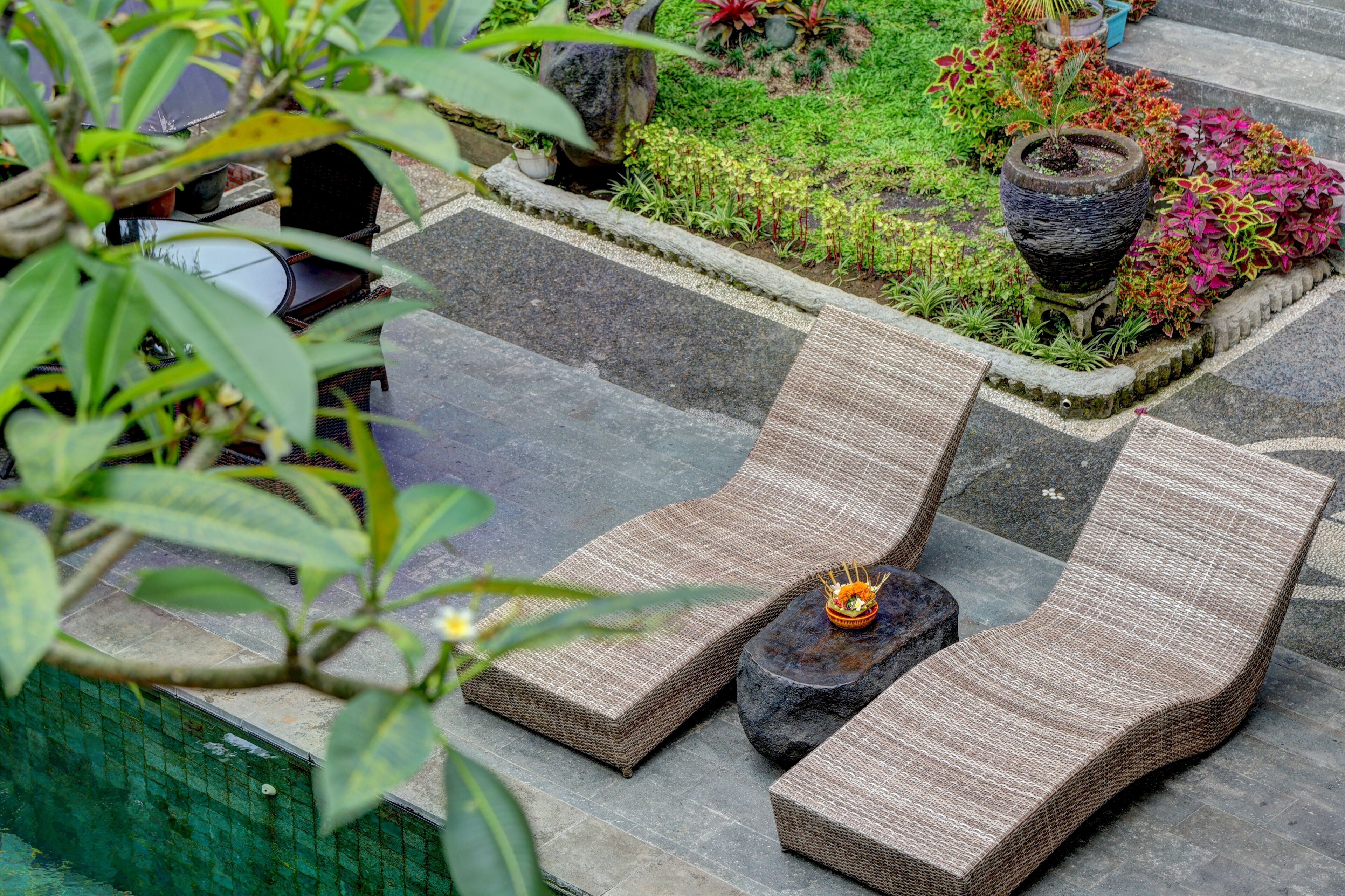 A garden area with a stone pathway, a seating area with wicker lounge chairs, and a small table with a bowl of flowers.