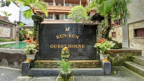 A guest house entrance with a stone facade, a pool, and tropical plants. - Kun - Kun Guest House Ubud (Ubud)