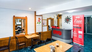 A hotel reception area with a wooden reception desk, several chairs, a large OYO promotional banner, and a mirror reflecting the interior. - OYO 437 Hostel Na Nara (Bangkok)