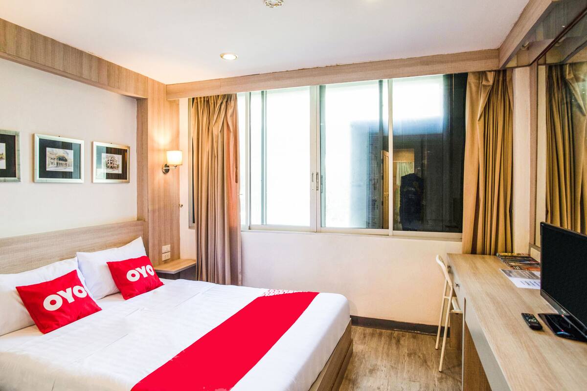 Une chambre d’hôtel avec un lit, un bureau, une télévision et une fenêtre avec des rideaux.
