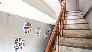 A staircase with wooden steps and metal railings, leading to a landing with a gray wall adorned with framed photographs. - OYO 437 Hostel Na Nara (Bangkok)