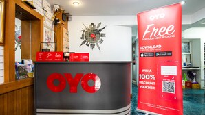 A reception desk with a large OYO logo, a globe artwork, and a promotional banner offering a 100% discount voucher. - OYO 437 Hostel Na Nara (Bangkok)