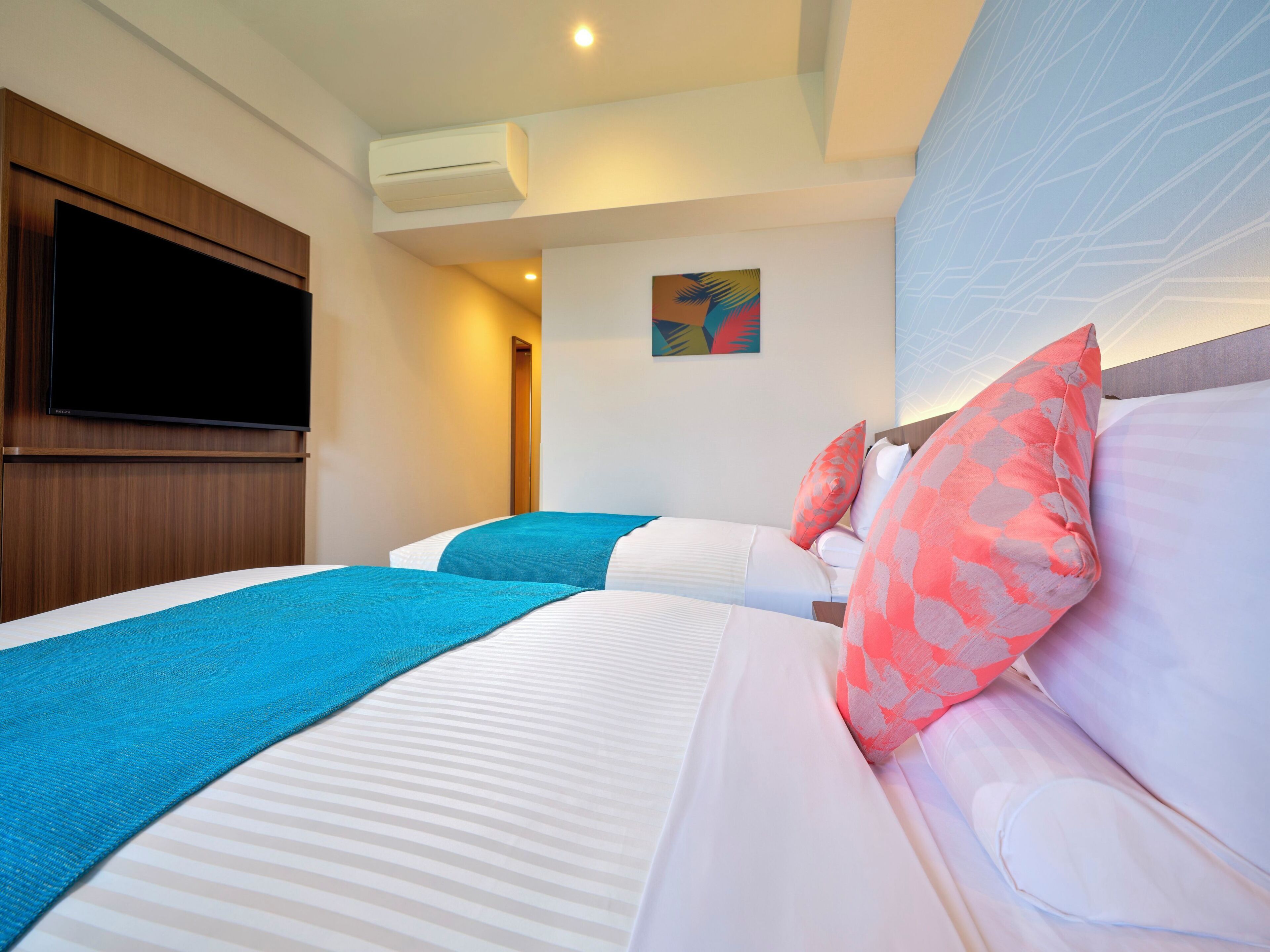 A hotel room with two beds, a flat-screen TV mounted on the wall, and an air conditioning unit.
