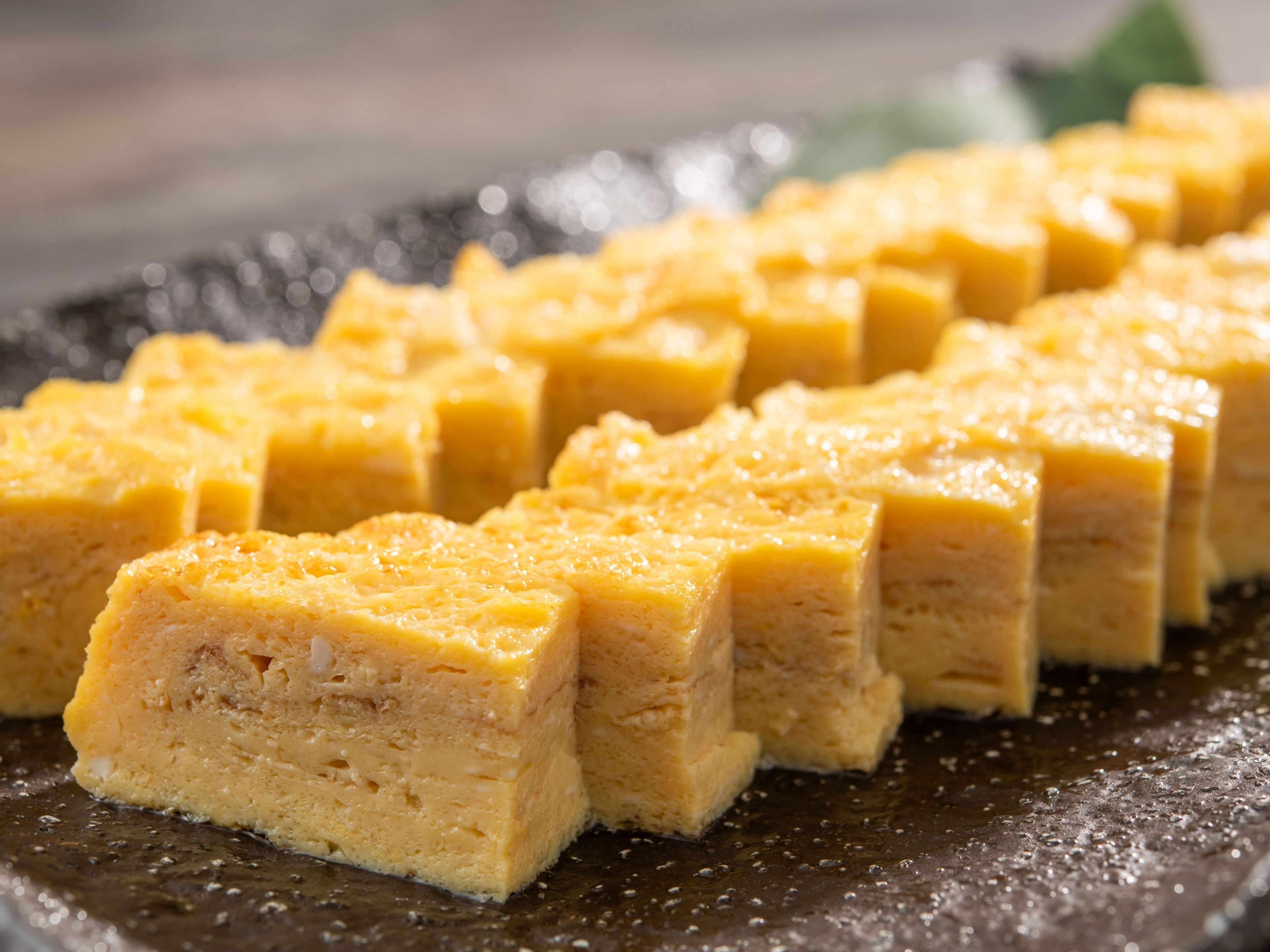 A close-up of a dessert with a textured surface, possibly a cake or pudding, on a dark plate.