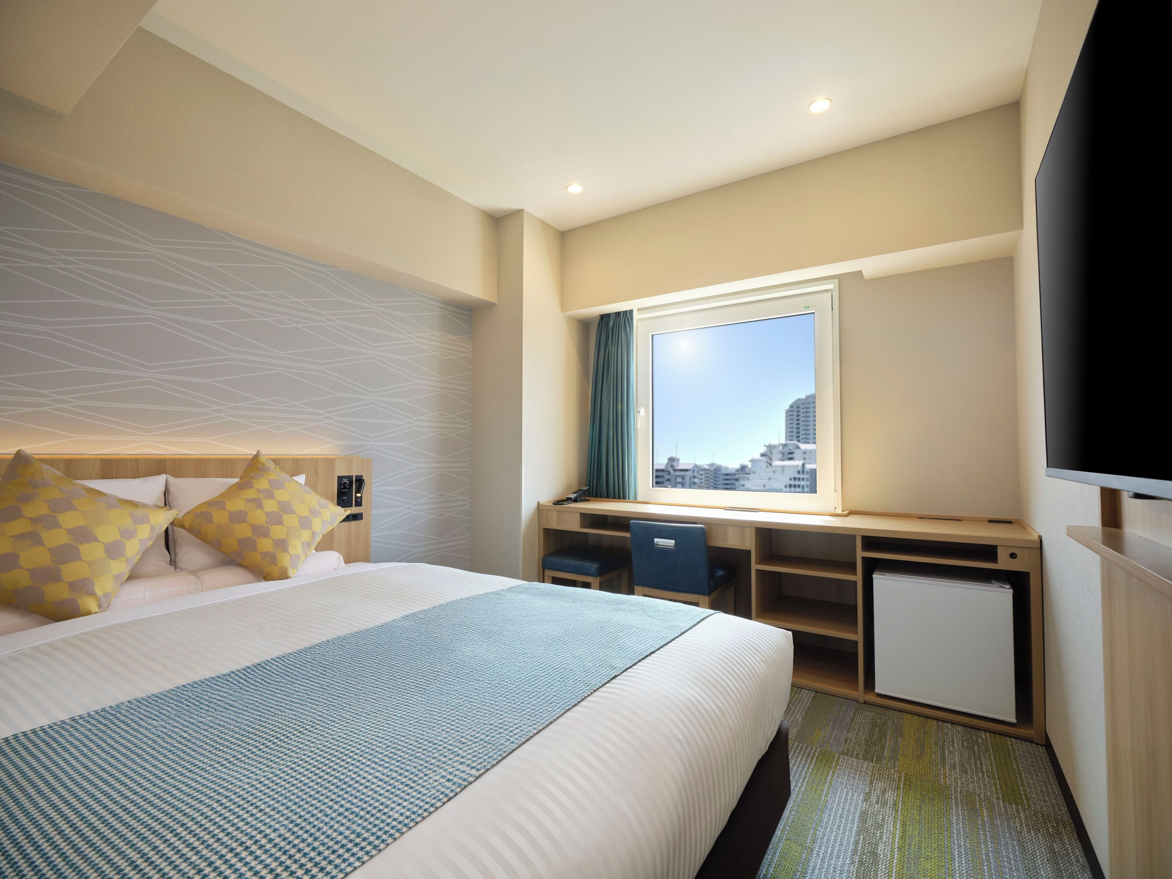 A hotel room with a bed, desk, chair, and a television.
