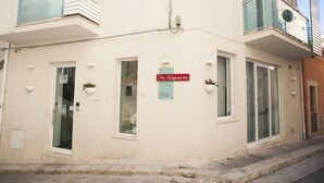 Um edifício com placa indicando o Ragusa Inn, apresentando porta de vidro, várias janelas e uma pequena varanda com plantas.