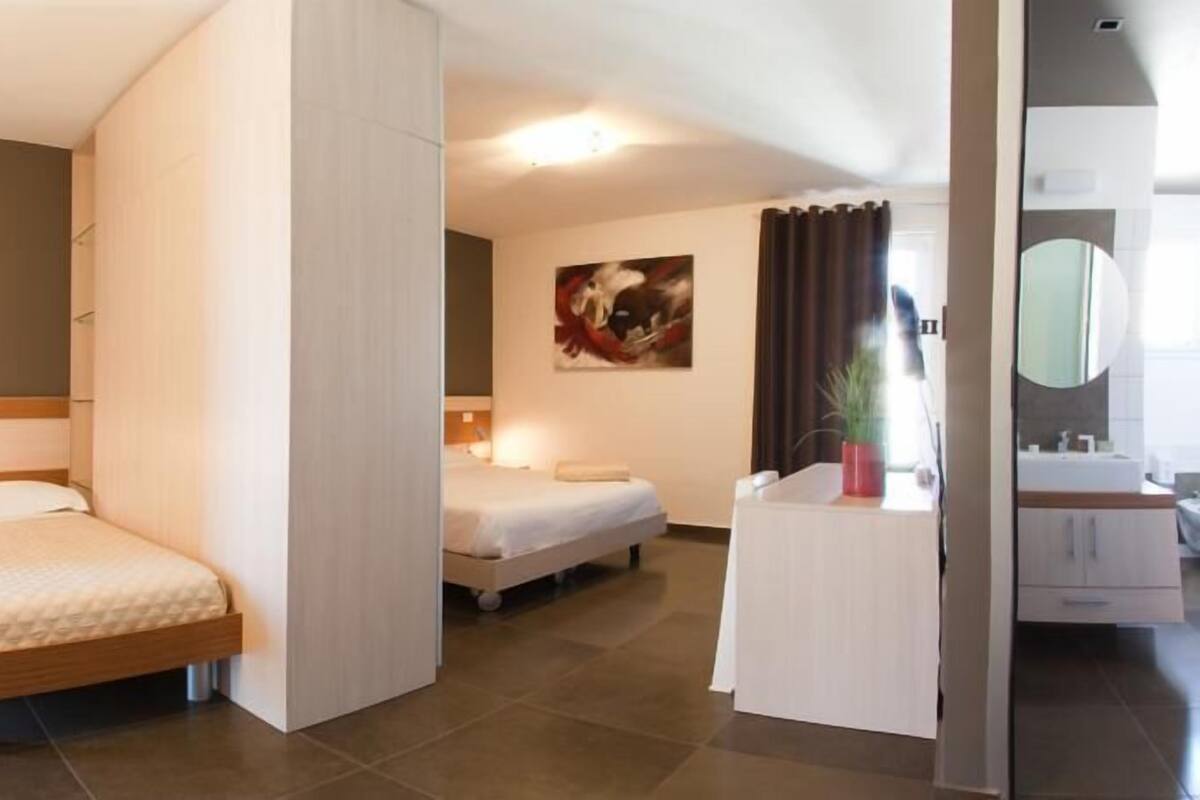 A modern hotel room with two beds, a bathroom with a mirror, and a painting on the wall.