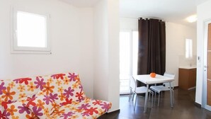 Um quarto com sofá estampado, mesa de jantar com cadeiras, pequena cozinha e janela com cortinas.