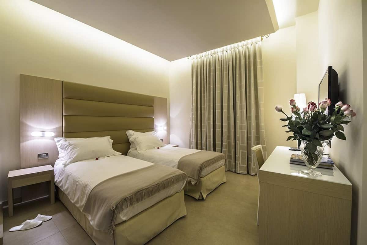 Habitación de hotel con dos camas, una mesita de noche, un escritorio con un florero y un ventanal con cortinas.