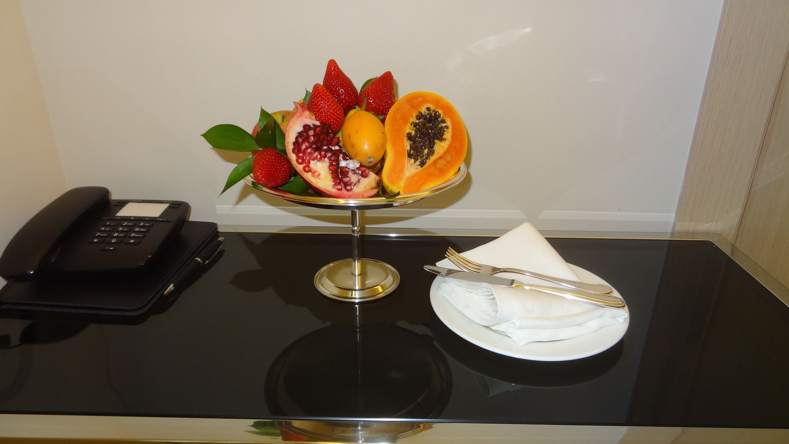 A table with a fruit bowl, a folded napkin, and a telephone.