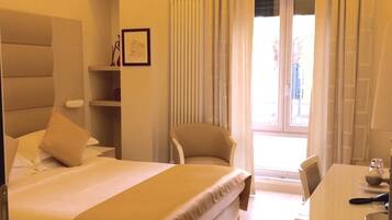 A hotel room with a large bed, a desk, a chair, and a window with curtains.