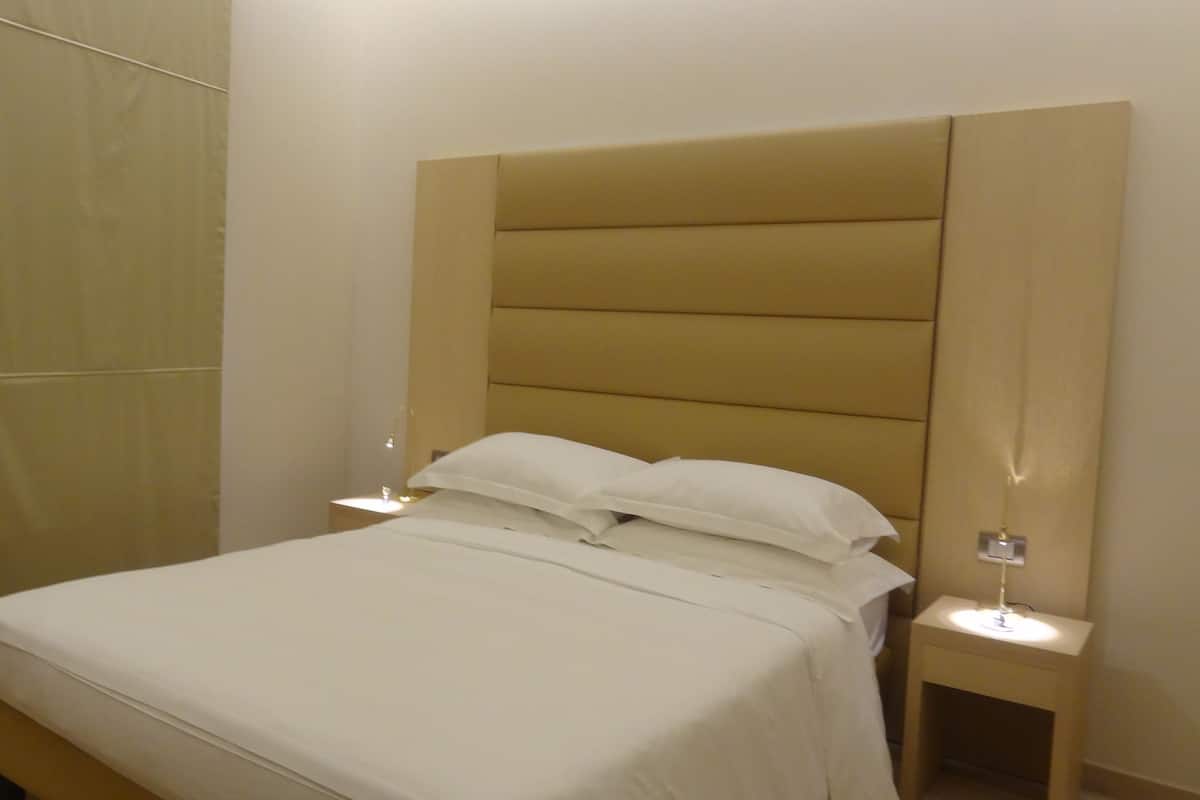 Una habitación de hotel con una cama grande, dos mesitas de noche con lámparas y un armario.