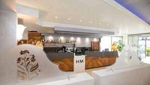 A modern hotel reception area with a bar, a counter with 'HM' signage, and a decorative plant. - Hotel Metropol (Chioggia)