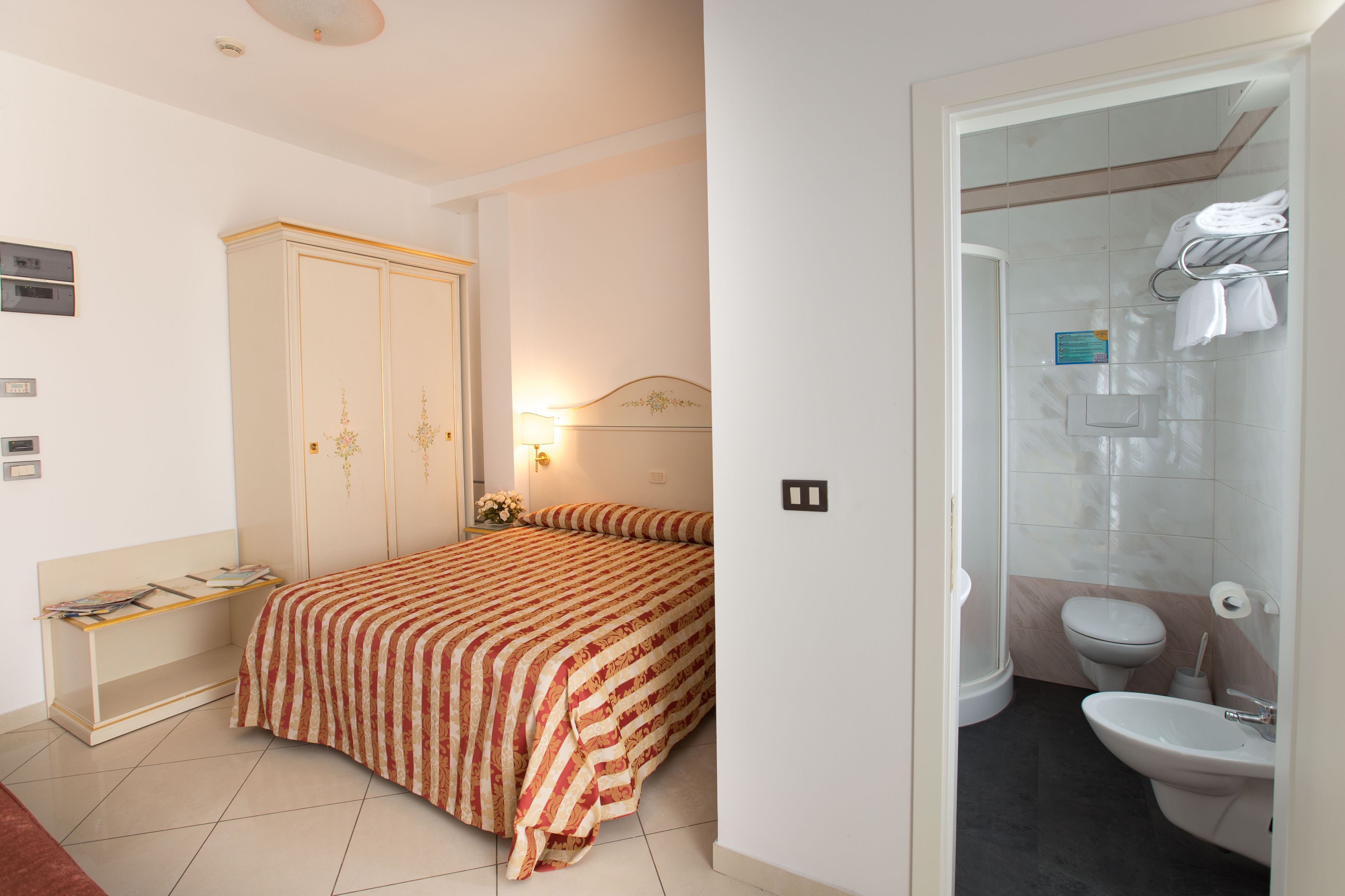 Una camera da letto con un letto, comodino, armadio e bagno completo di toilette, lavandino e doccia.