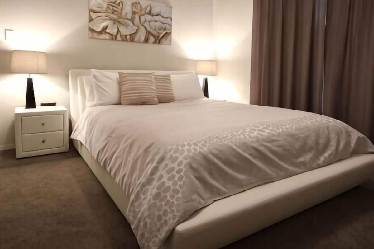 Una cama bien hecha con una colcha estampada, dos lámparas de noche y una mesita de noche con cajones.