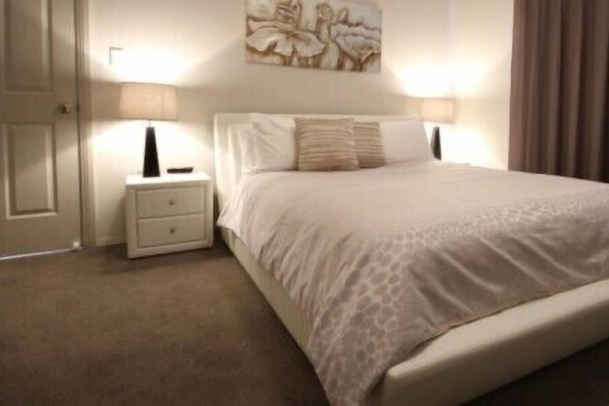 Un dormitorio ordenado con una cama grande, dos mesitas de noche y una obra de arte colgada en la pared.