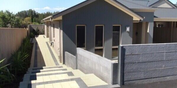 A residential building with a grey facade, a front entrance with a door and windows, and a concrete pathway leading to the entrance. - Casavino Luxury Villas (McLaren Vale)