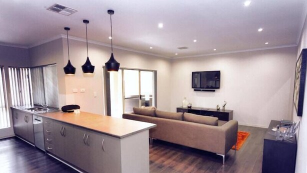 A modern kitchen with a central island, a dining area with a sofa, and a flat-screen TV mounted on the wall.