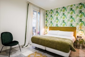 Ein Schlafzimmer mit Bett, einem Sessel, einem Fenster mit Vorhängen und einer Wand mit einem Blattmuster.
