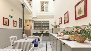 Un comedor con manteles a rayas, sillas blancas, una encimera de cocina con plantas y cuadros en las paredes.