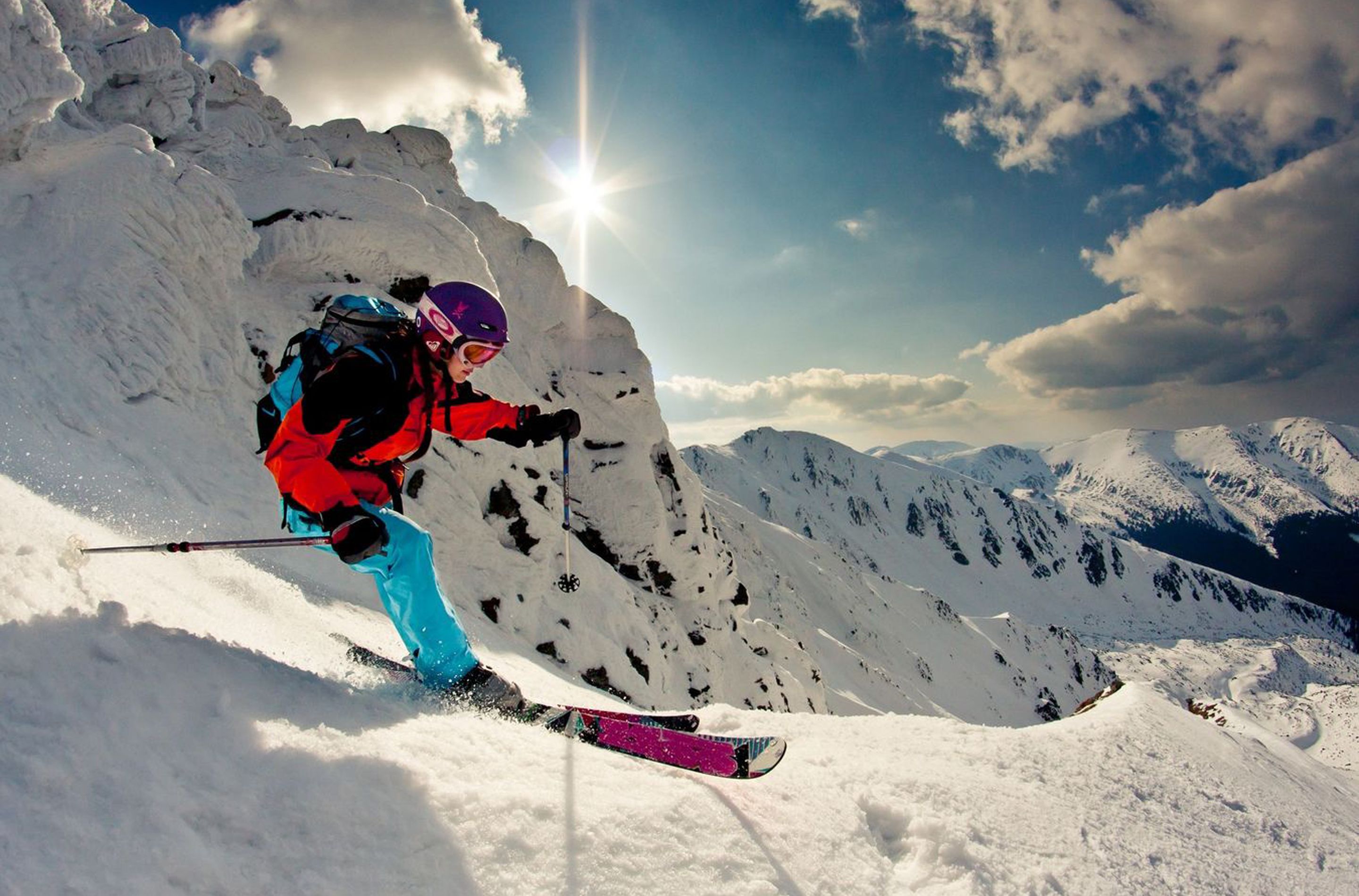 A skier on a snowy mountain slope with a clear sky and distant mountains.