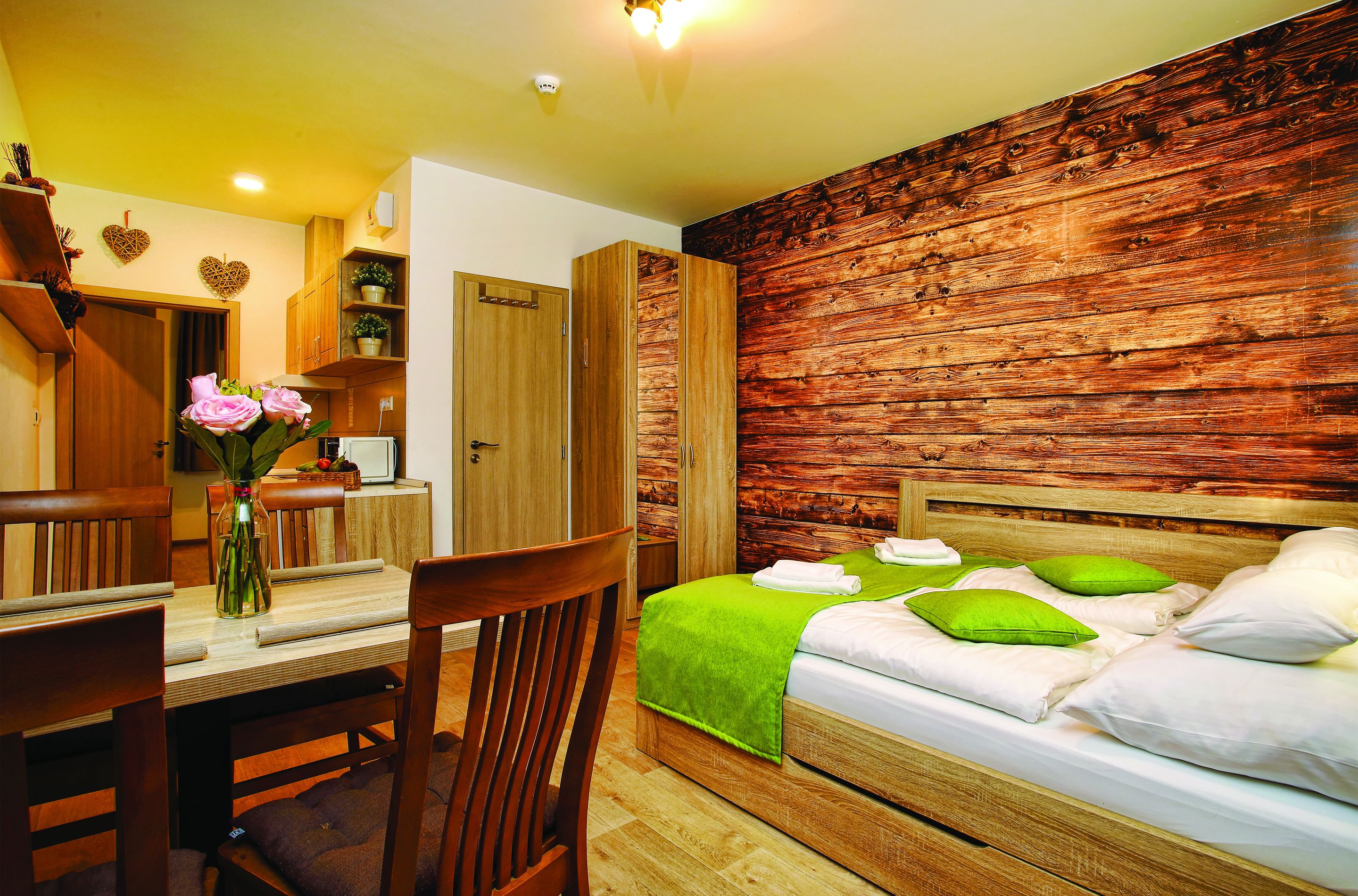Un dormitorio con cabecera de madera, colcha verde y una mesa de comedor de madera con sillas.