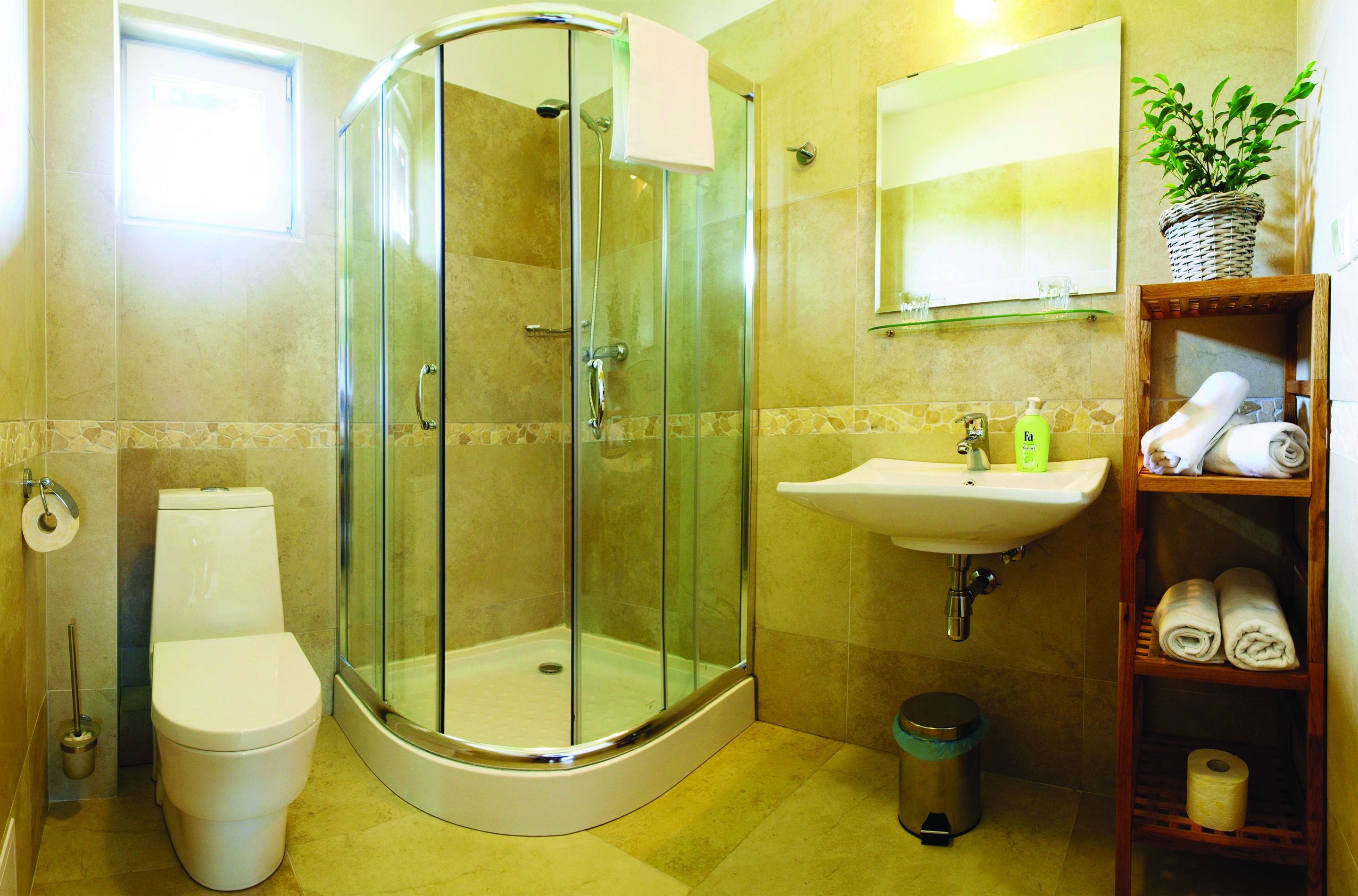 A bathroom with a glass-enclosed shower, a toilet, a sink, and a shelf with towels.