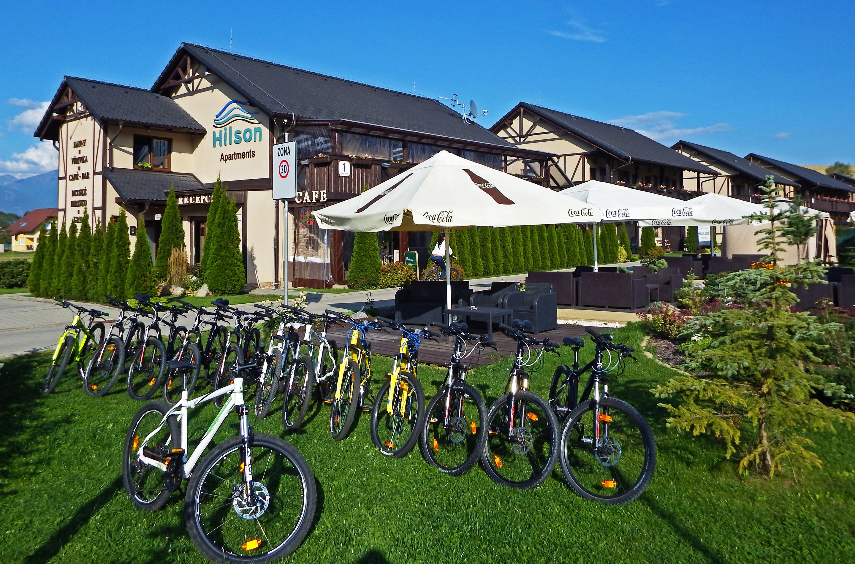 A hotel with a row of bicycles parked outside, a cafe, and outdoor seating with umbrellas.