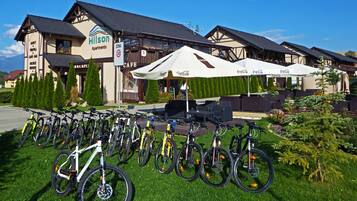 A hotel with a row of bicycles parked outside, a cafe, and outdoor seating with umbrellas.