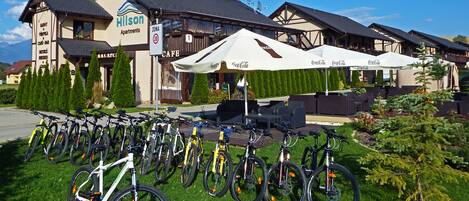 Un hotel con una fila de bicicletas estacionadas afuera, una cafetería y asientos exteriores con sombrillas.