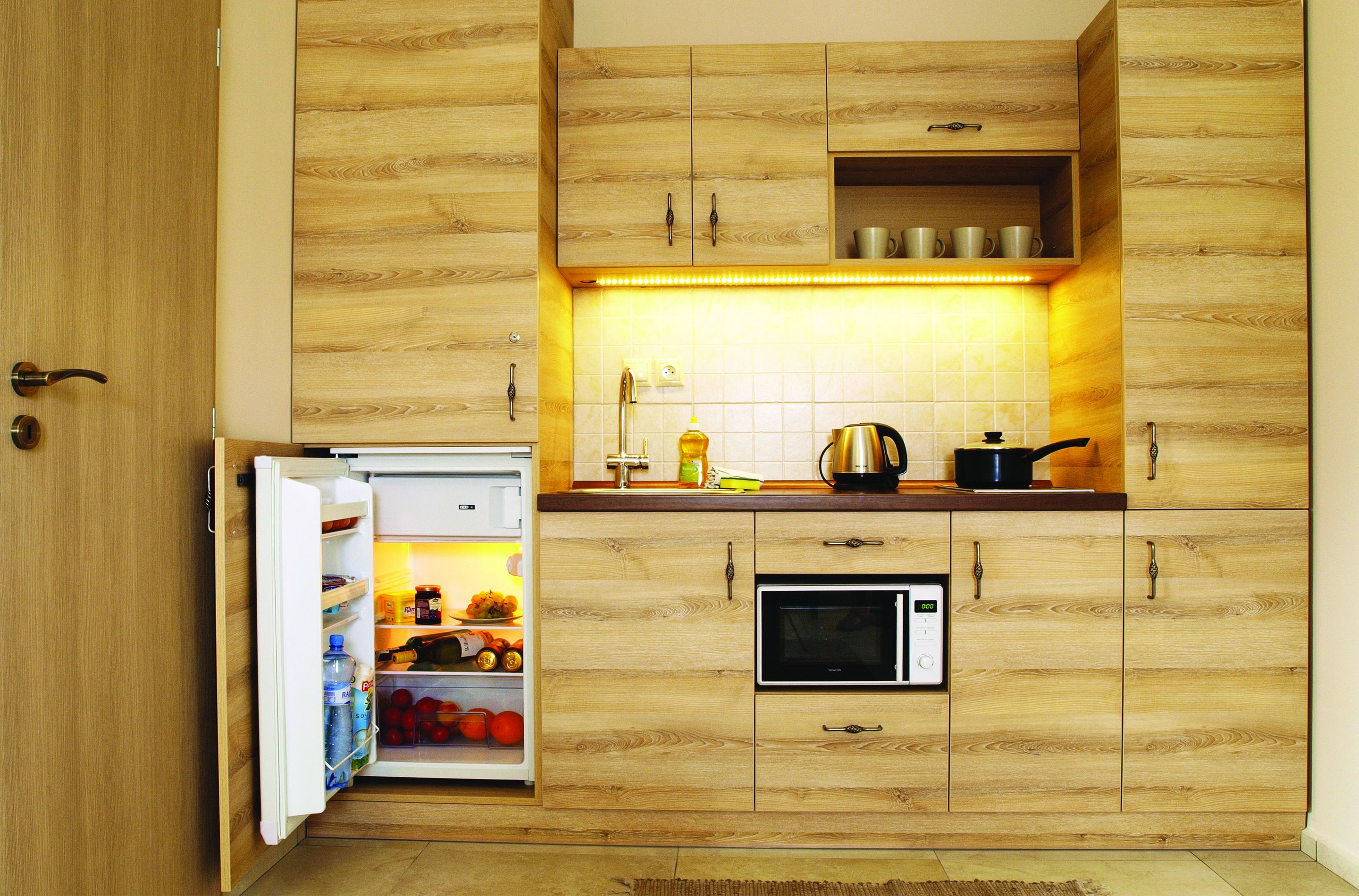 Una cocina compacta con armarios de madera, un microondas integrado y un refrigerador.