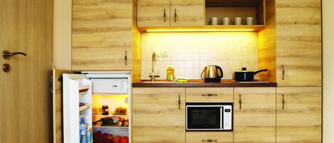 Una cocina compacta con armarios de madera, un microondas integrado y un refrigerador.