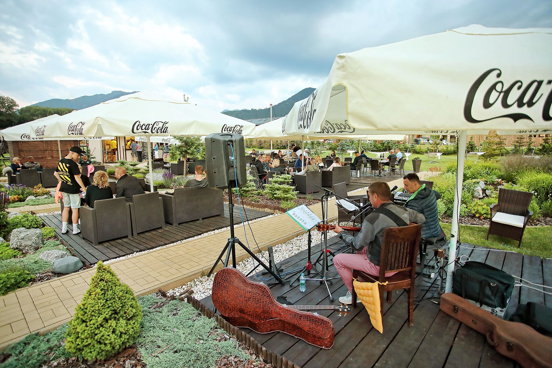 Zona exterior con mesas y sillas bajo sombrillas, una guitarra y equipo de sonido.