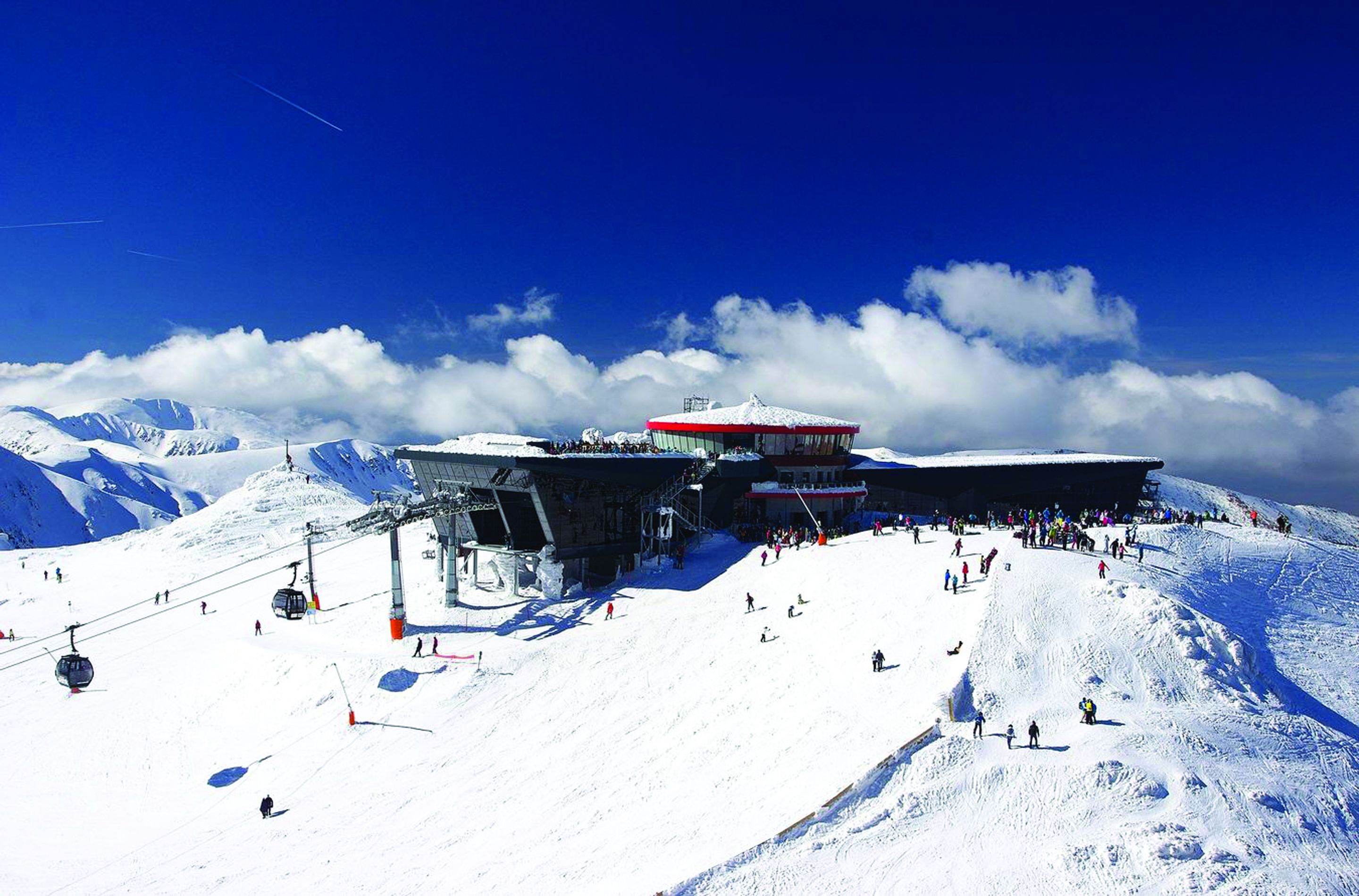 A ski resort with a chairlift, a ski lift tower, and a snowy mountain backdrop.