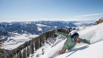 A snowboarder on a snowy mountain with a clear view of distant mountains and forests.