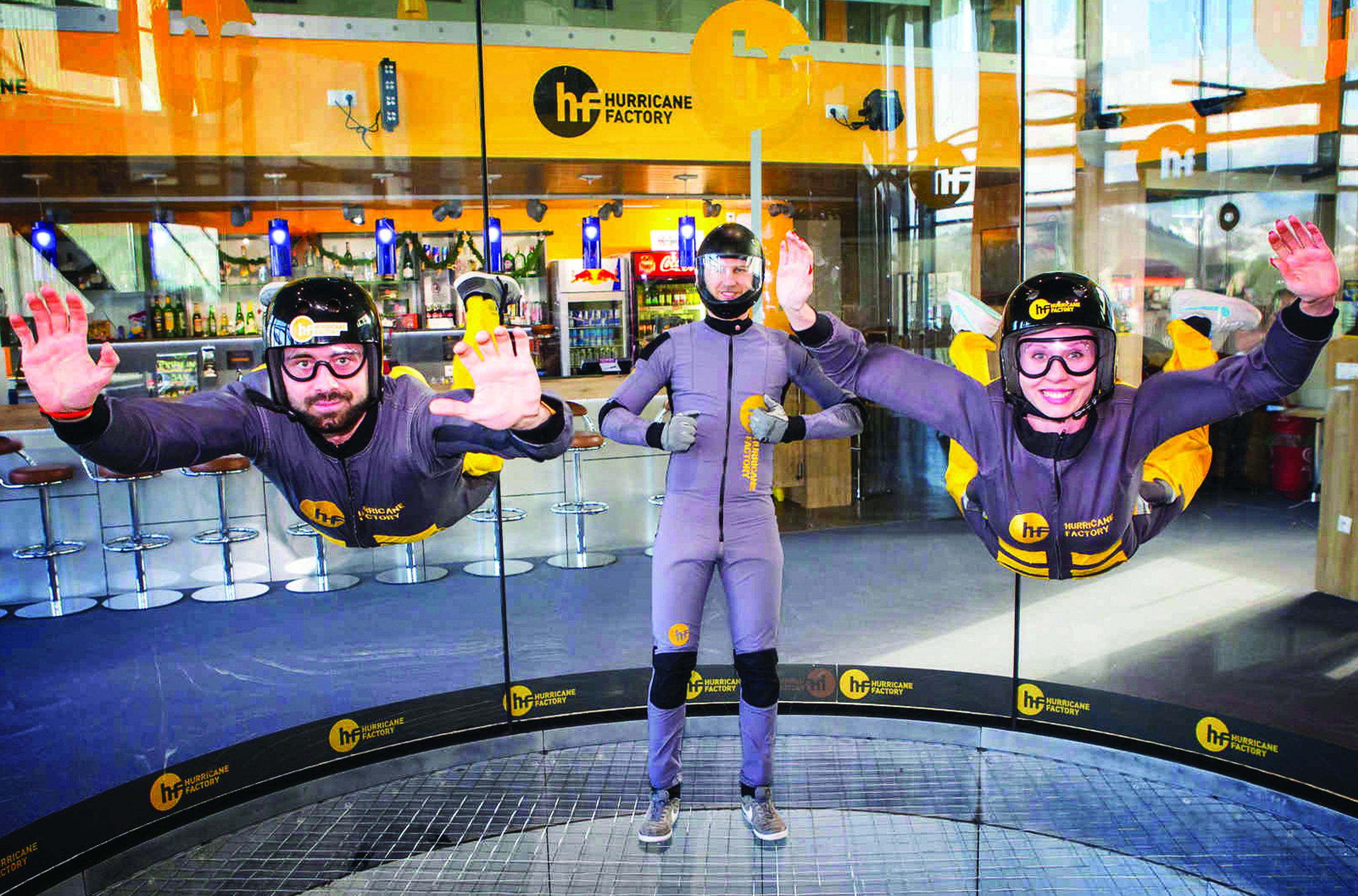 Three people in a circular glass enclosure with a Hurricane Factory sign in the background.