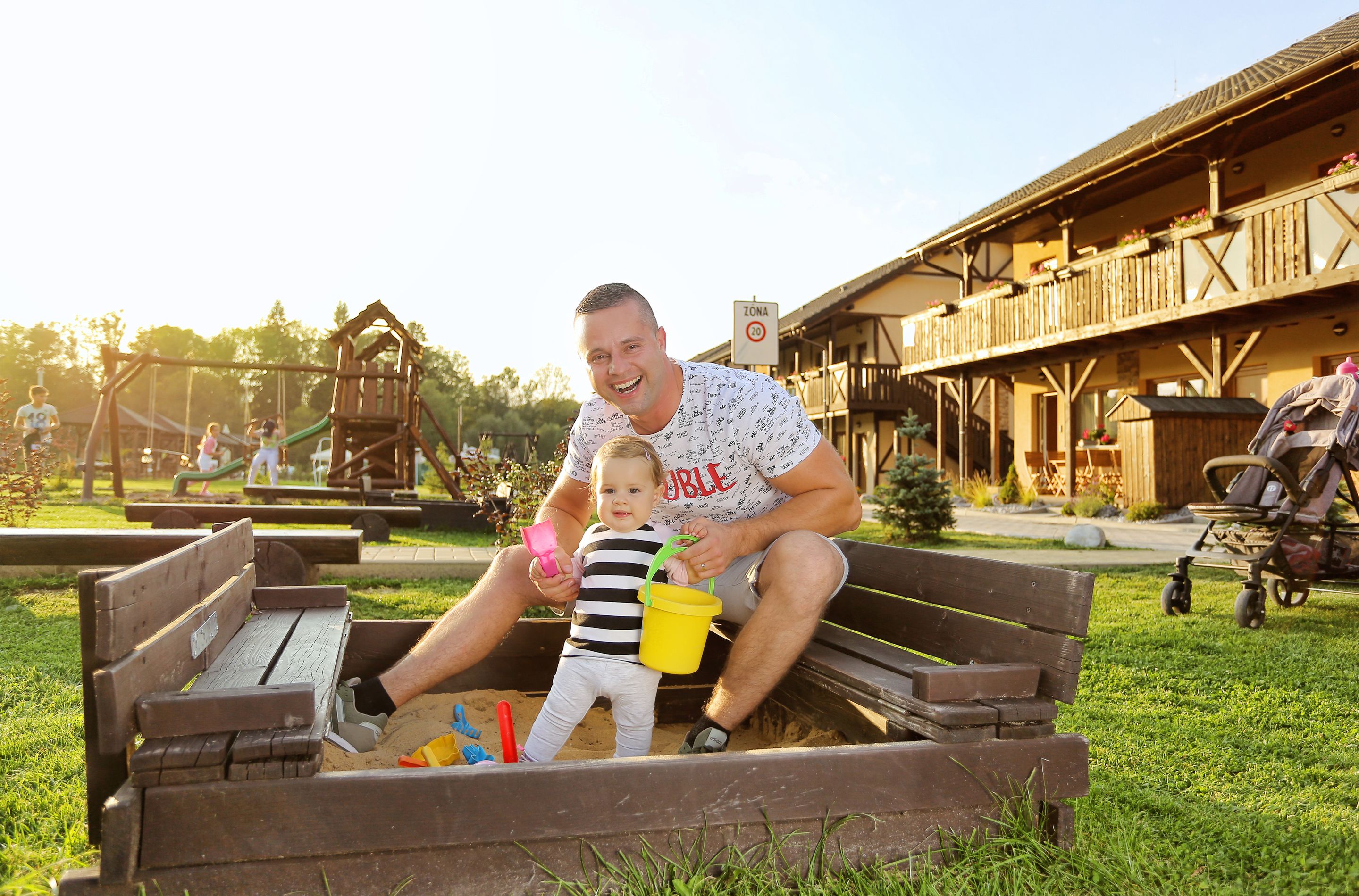 A wooden play structure in a park with a building in the background.