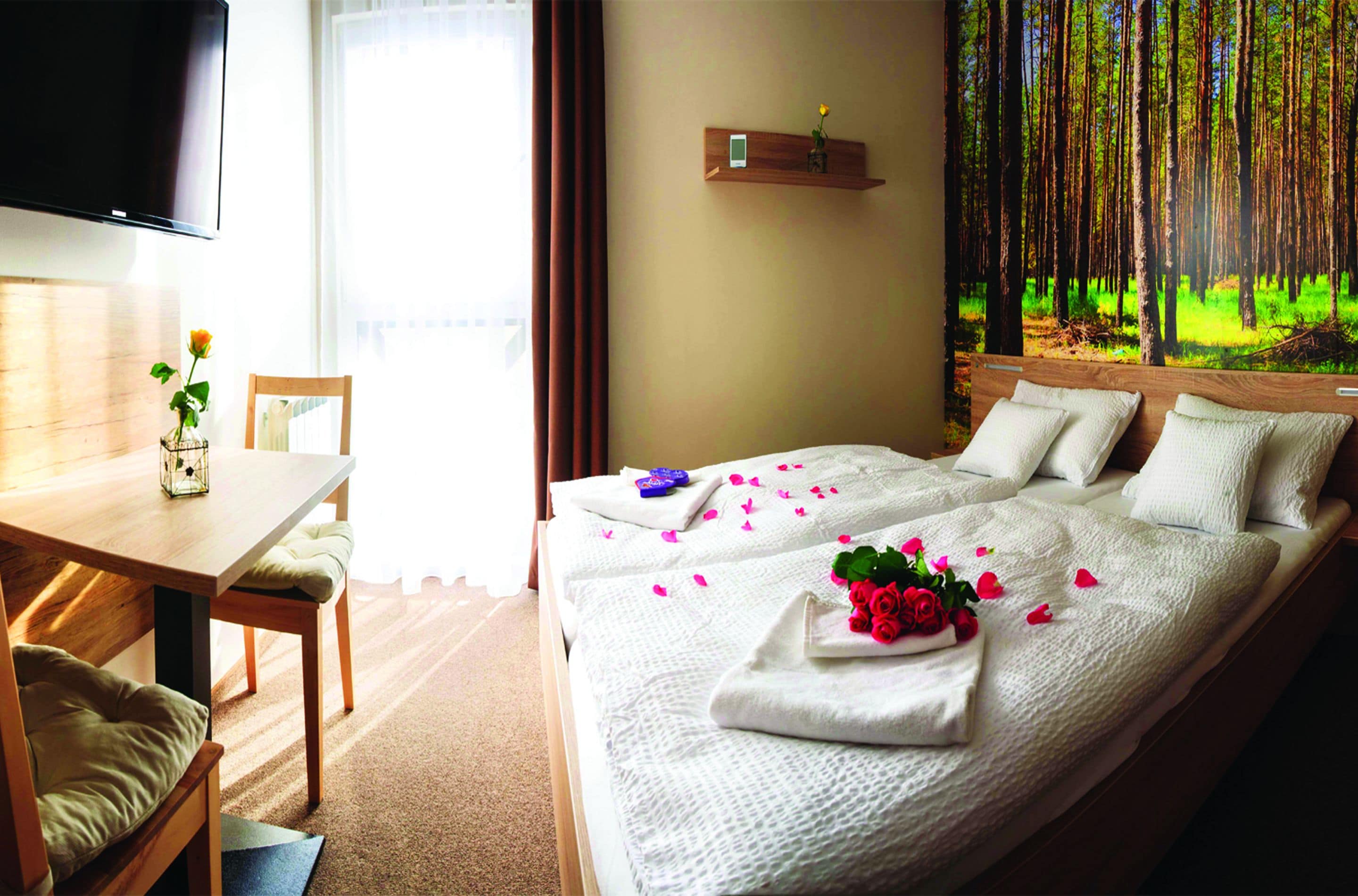 Une chambre d’hôtel avec un lit, un bureau, une chaise, une télévision et une étagère fixée au mur, sur laquelle est posée une fleur.