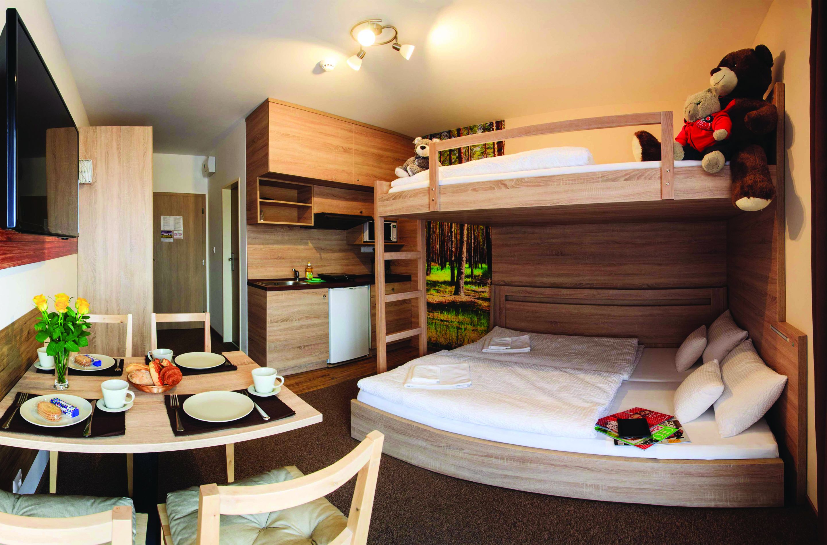 A bunk bed room with a desk, kitchenette, and a dining area.