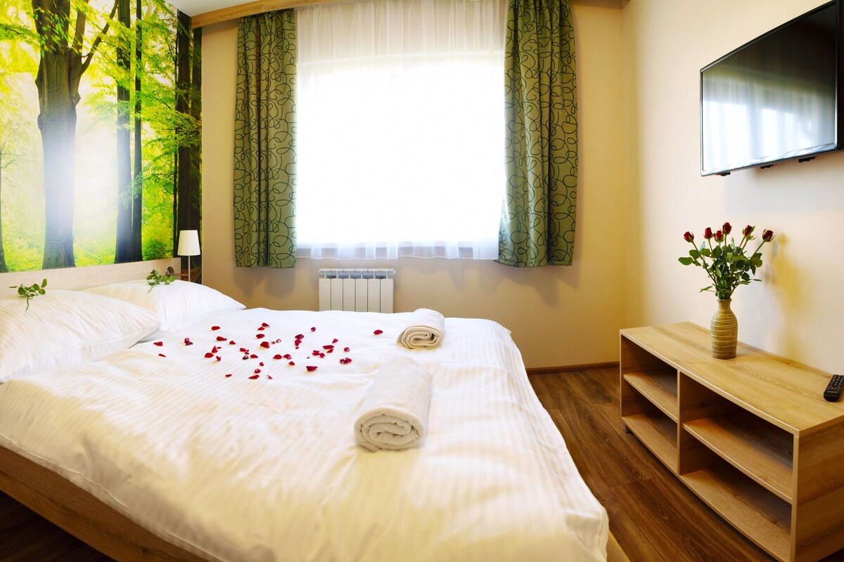 A hotel room with a bed, a TV mounted on the wall, and a window with curtains.