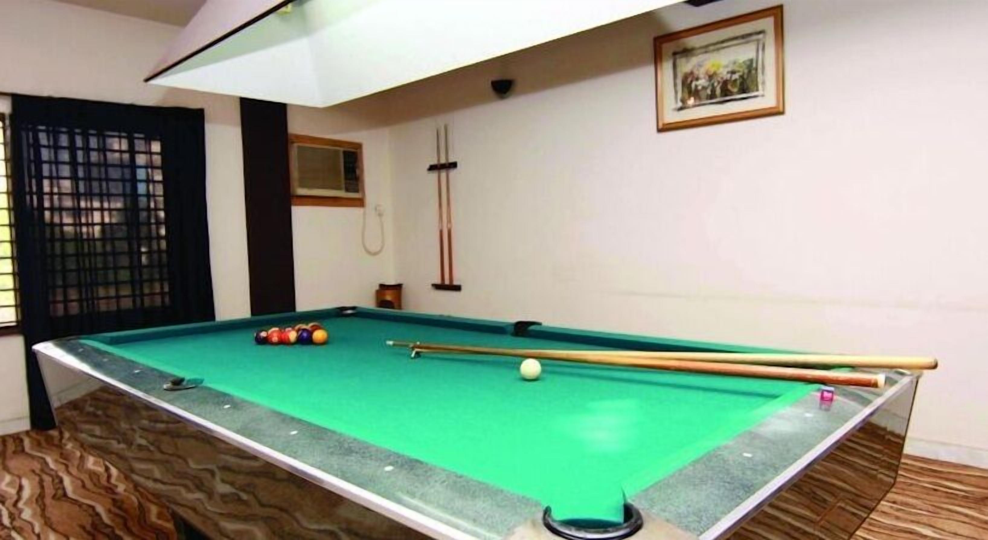 Una mesa de billar con bolas y tacos, una ventana con persianas, y un cuadro en la pared.