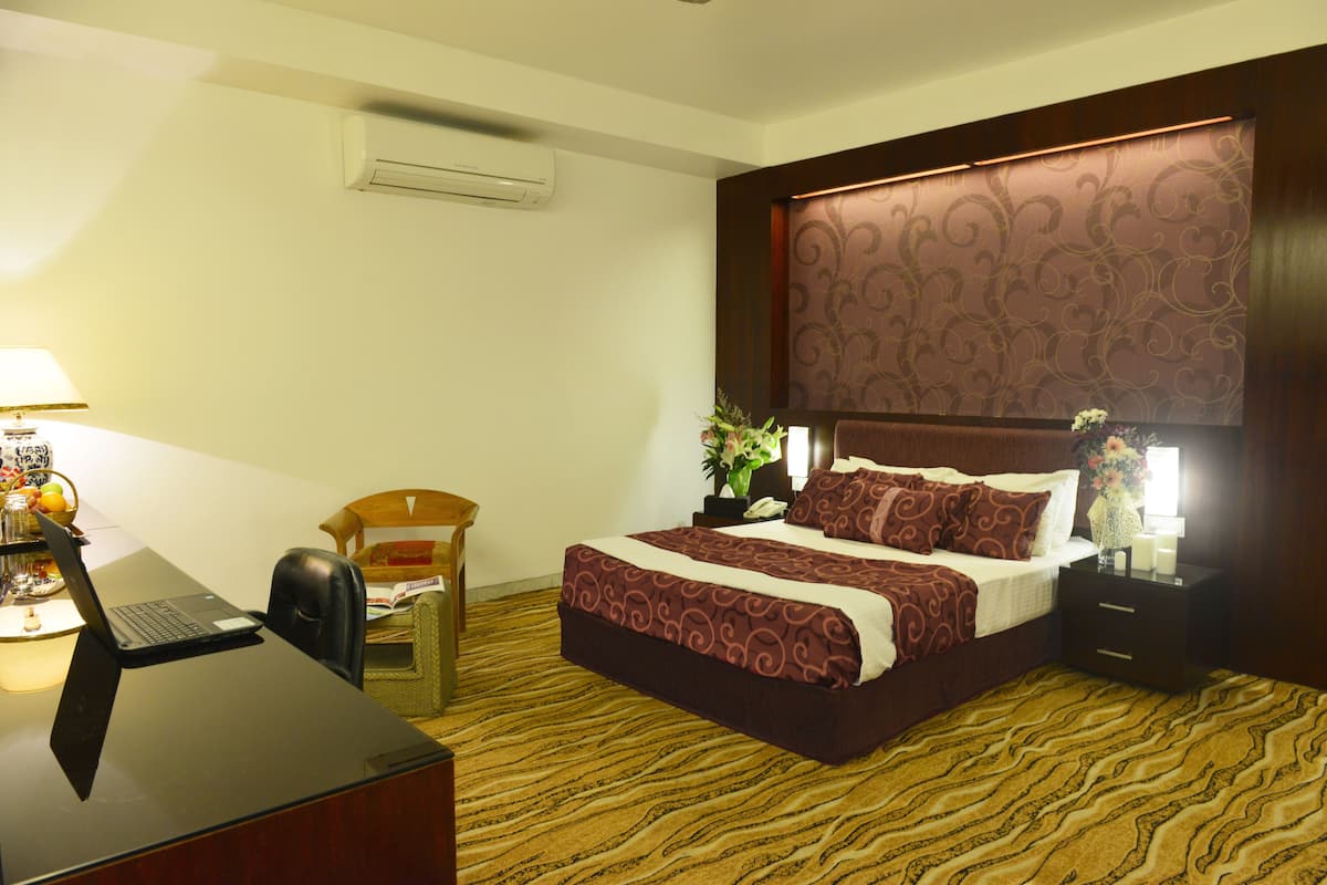Une chambre d’hôtel comprenant un lit, un bureau avec un ordinateur portable, une chaise, une table de chevet avec une lampe et un climatiseur fixé au mur.