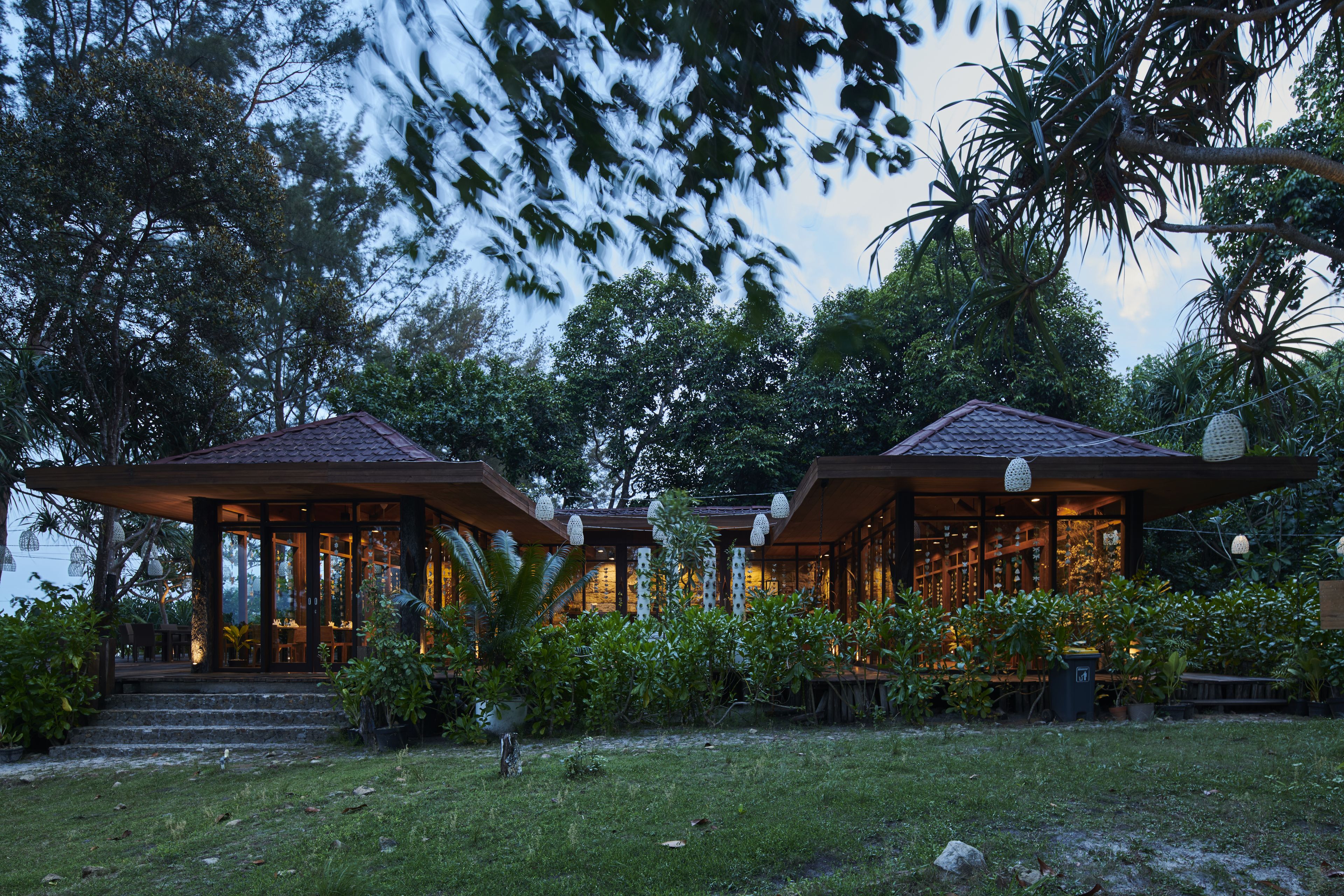 A two-story building with a tiled roof, surrounded by lush greenery and trees.