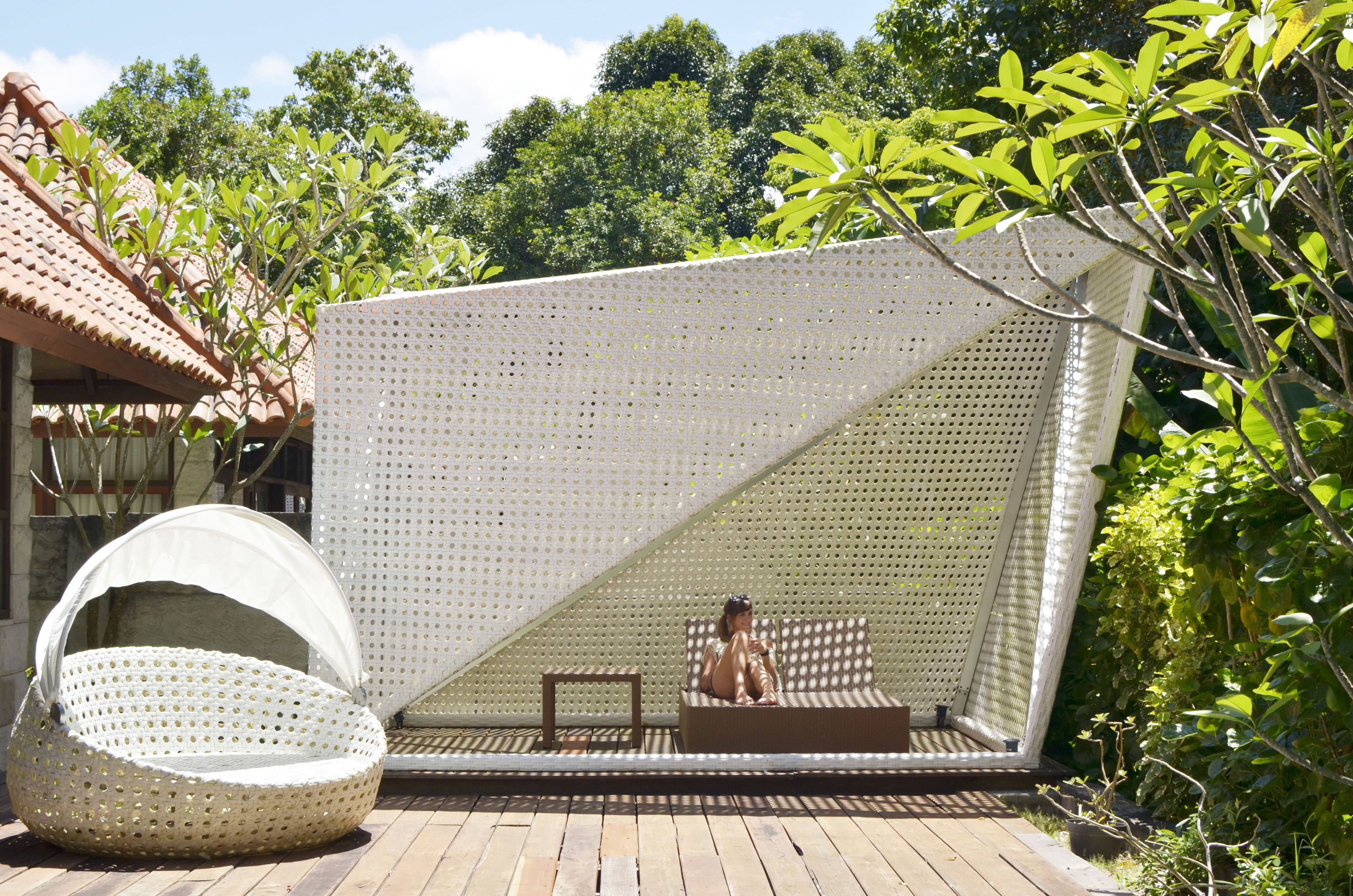 A sunlit outdoor seating area with a perforated screen, a woven chair, and a wooden deck.