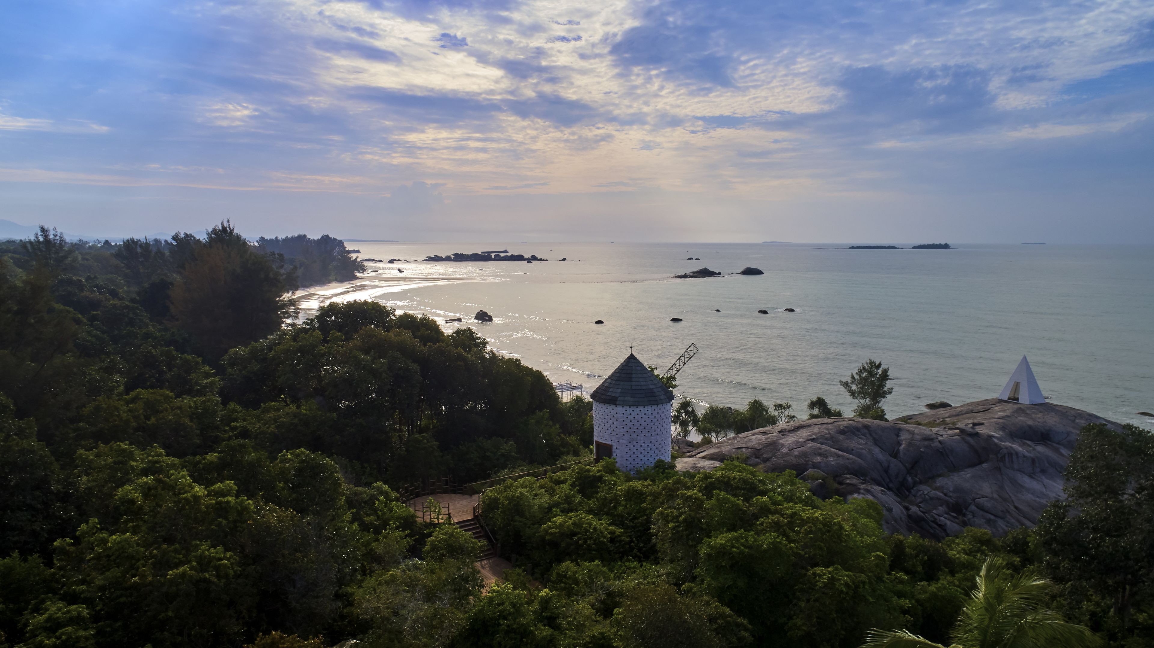 Un paisaje costero con un faro, abundante vegetación y un mar tranquilo.