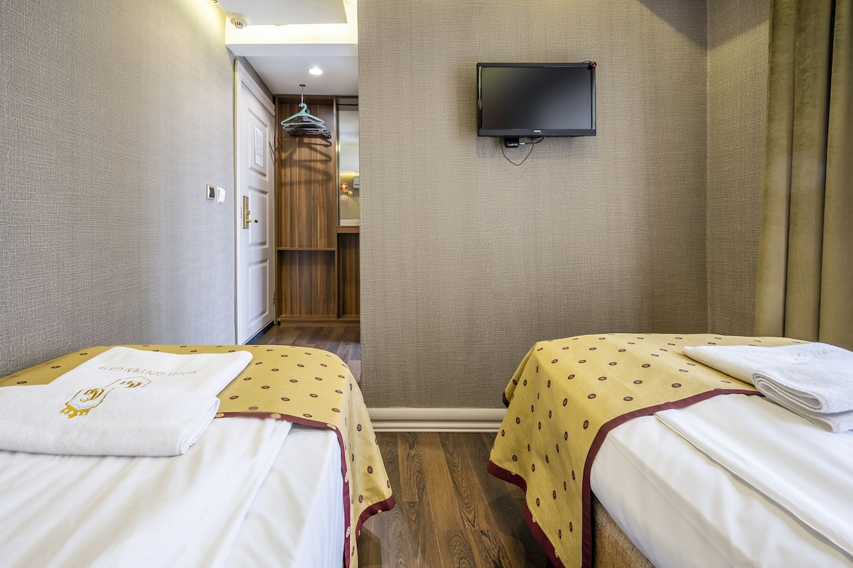 A hotel room with two beds, a television mounted on the wall, and a wooden wardrobe.