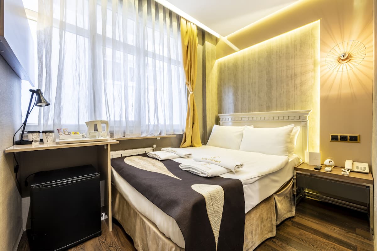 A hotel room with a bed, bedside table, lamp, and a desk with a computer and a coffee cup.