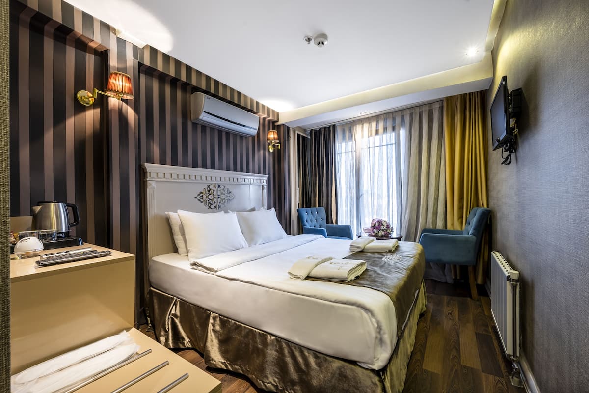 A hotel room with a large bed, a desk with a coffee maker, a TV mounted on the wall, and a chair.