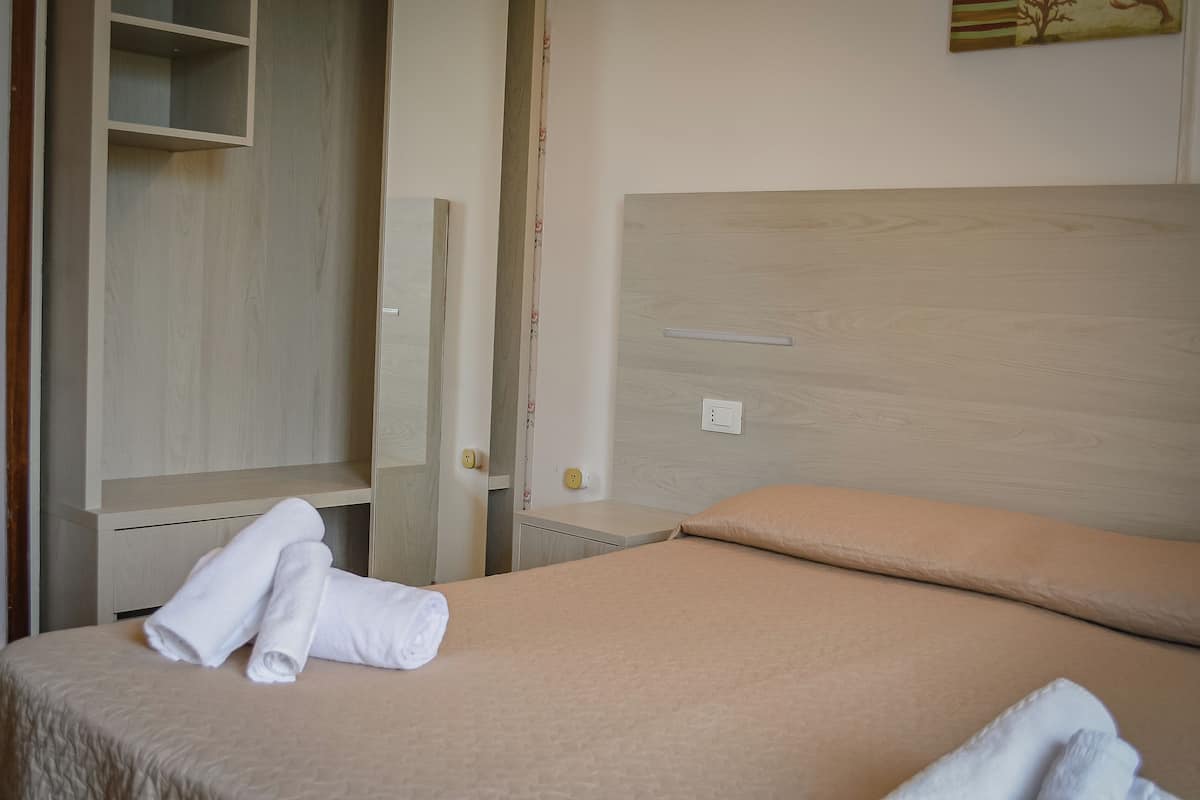 A hotel room with a bed, a wardrobe, and a wall-mounted shelf.